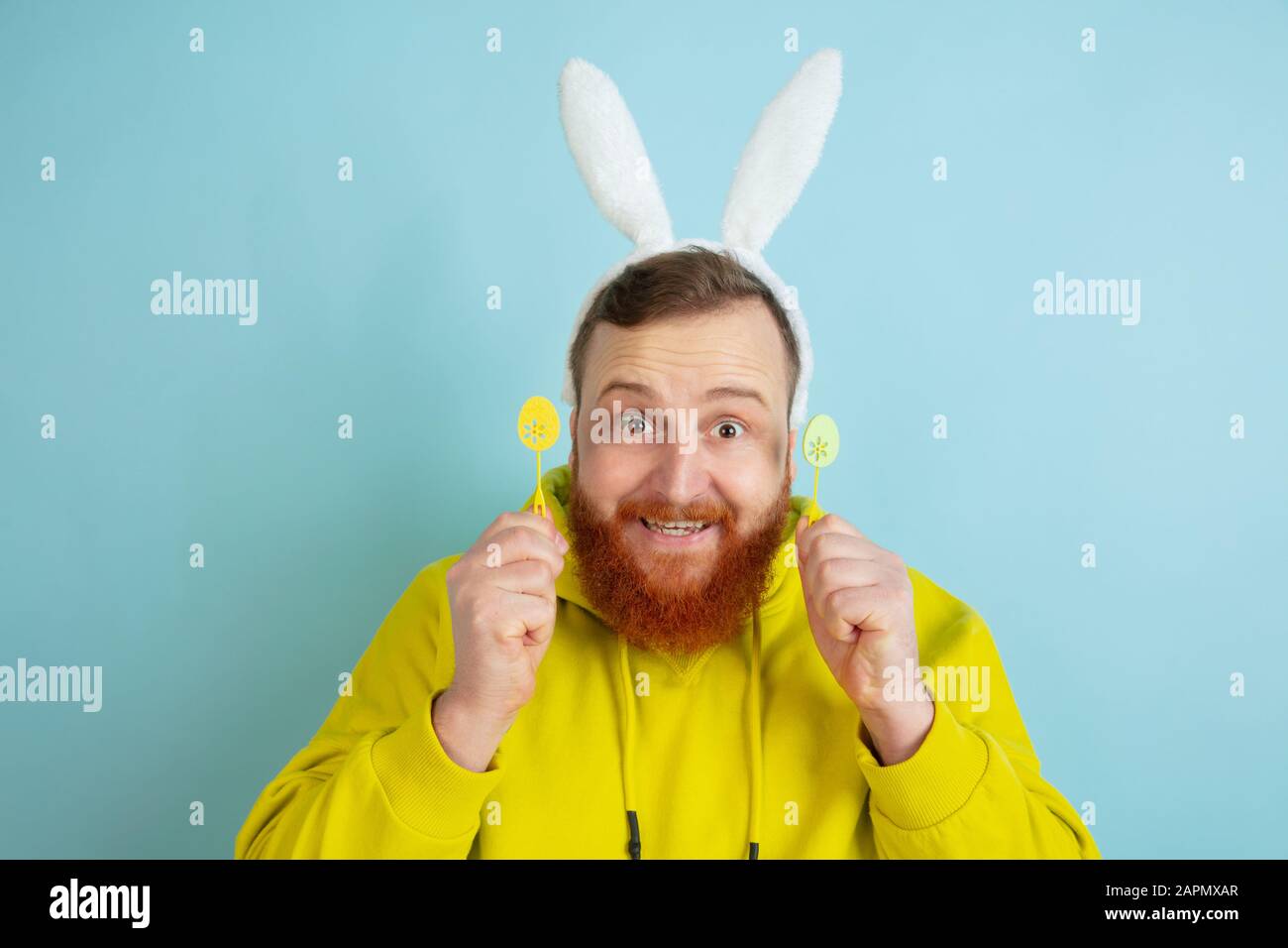 Homme caucasien au décor traditionnel comme lapin de Pâques avec des vêtements clairs et décontractés sur fond de studio bleu. Joyeuses salutations de pâques. Concept d'émotions humaines, d'expression faciale, de vacances. Copyspace. Banque D'Images