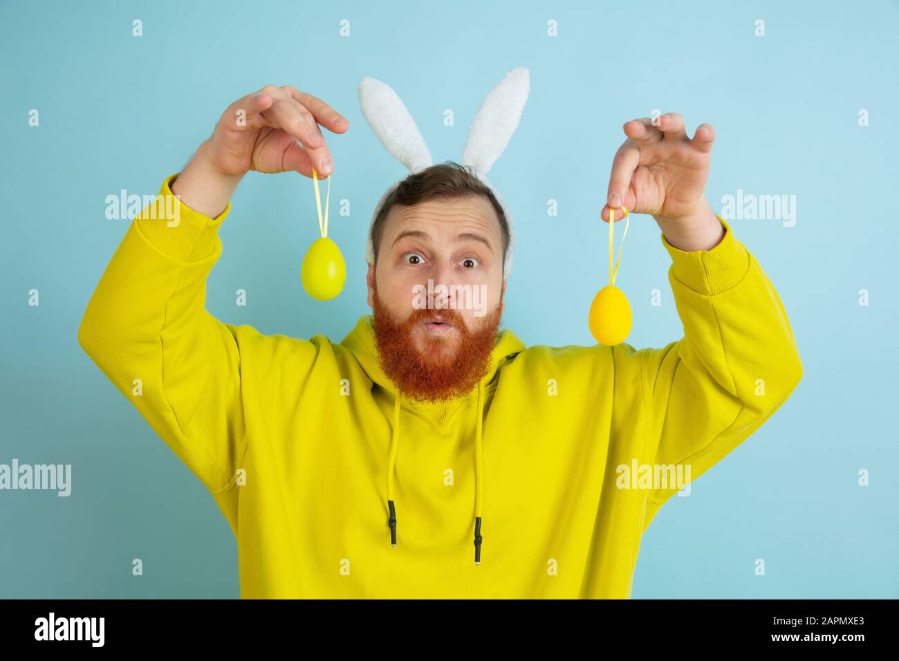 Chasse aux œufs à venir. Homme caucasien comme lapin de Pâques avec des vêtements décontractés lumineux sur fond bleu studio. Joyeuses salutations de pâques. Concept d'émotions humaines, d'expression faciale, de vacances. Copyspace. Banque D'Images