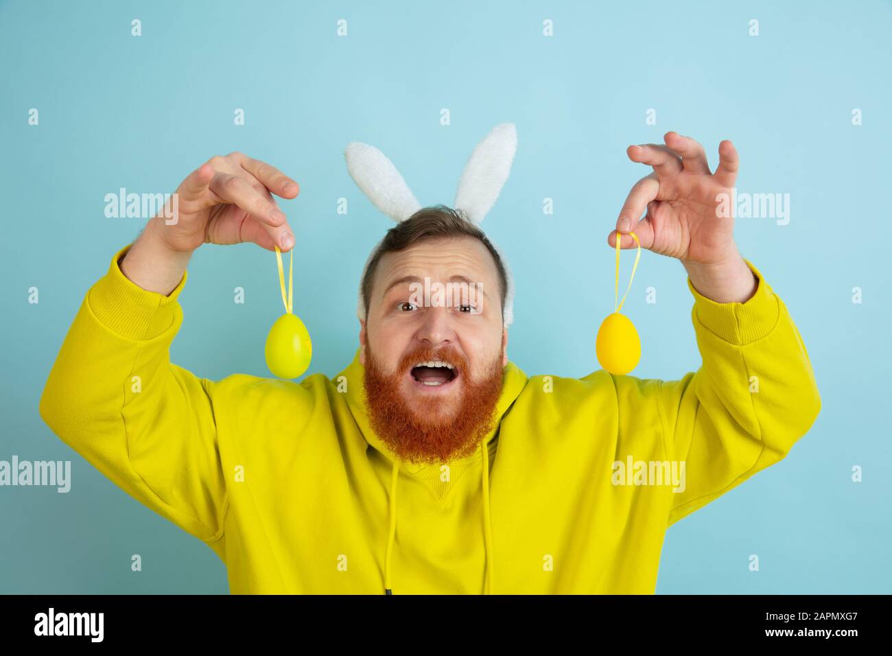 Chasse aux œufs à venir. Homme caucasien comme lapin de Pâques avec des vêtements décontractés lumineux sur fond bleu studio. Joyeuses salutations de pâques. Concept d'émotions humaines, d'expression faciale, de vacances. Copyspace. Banque D'Images
