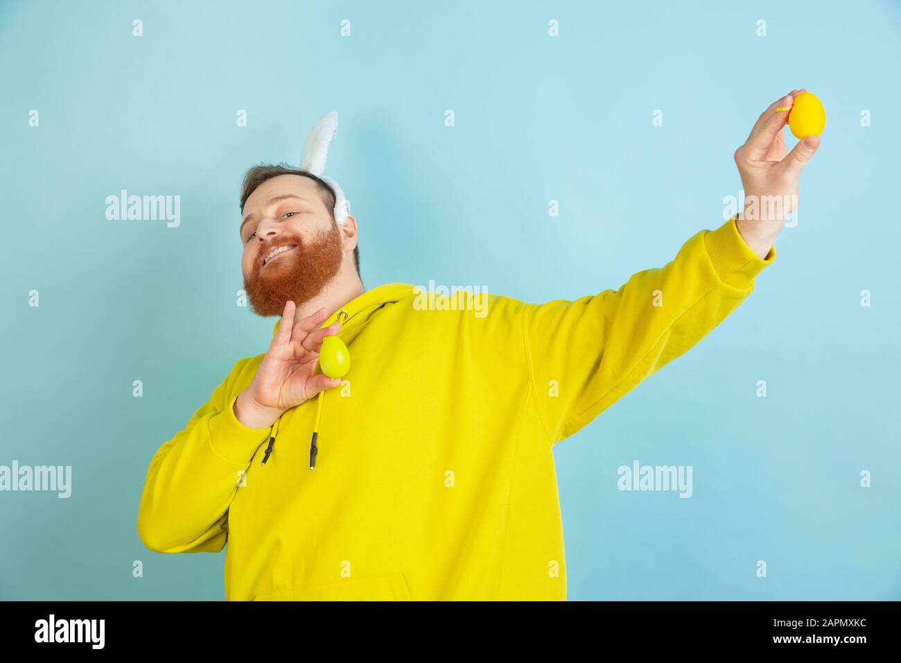 Chasse aux œufs à venir. Homme caucasien comme lapin de Pâques avec des vêtements décontractés lumineux sur fond bleu studio. Joyeuses salutations de pâques. Concept d'émotions humaines, d'expression faciale, de vacances. Copyspace. Banque D'Images