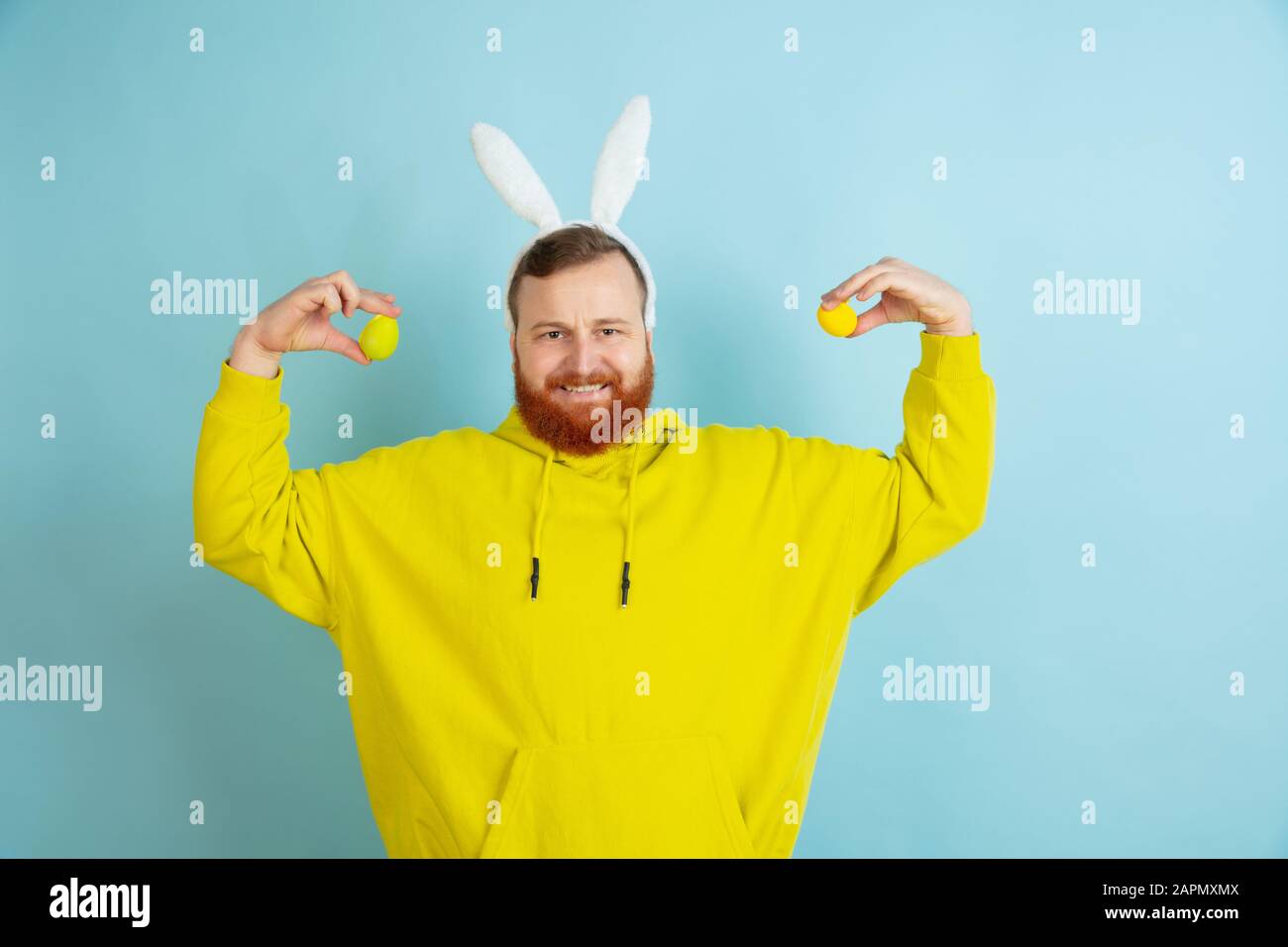 Chasse aux œufs à venir. Homme caucasien comme lapin de Pâques avec des vêtements décontractés lumineux sur fond bleu studio. Joyeuses salutations de pâques. Concept d'émotions humaines, d'expression faciale, de vacances. Copyspace. Banque D'Images