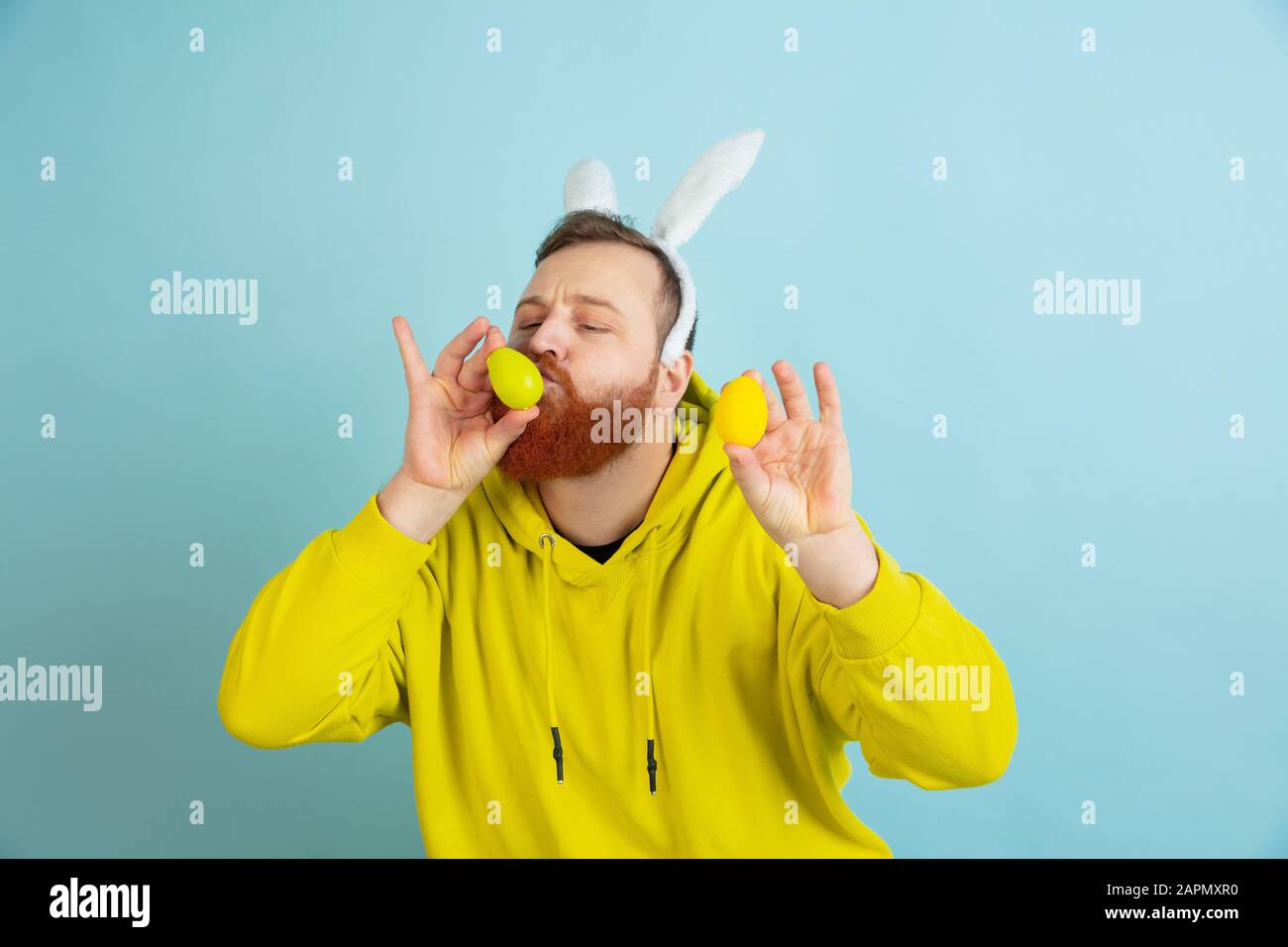 Chasse aux œufs à venir. Homme caucasien comme lapin de Pâques avec des vêtements décontractés lumineux sur fond bleu studio. Joyeuses salutations de pâques. Concept d'émotions humaines, d'expression faciale, de vacances. Copyspace. Banque D'Images