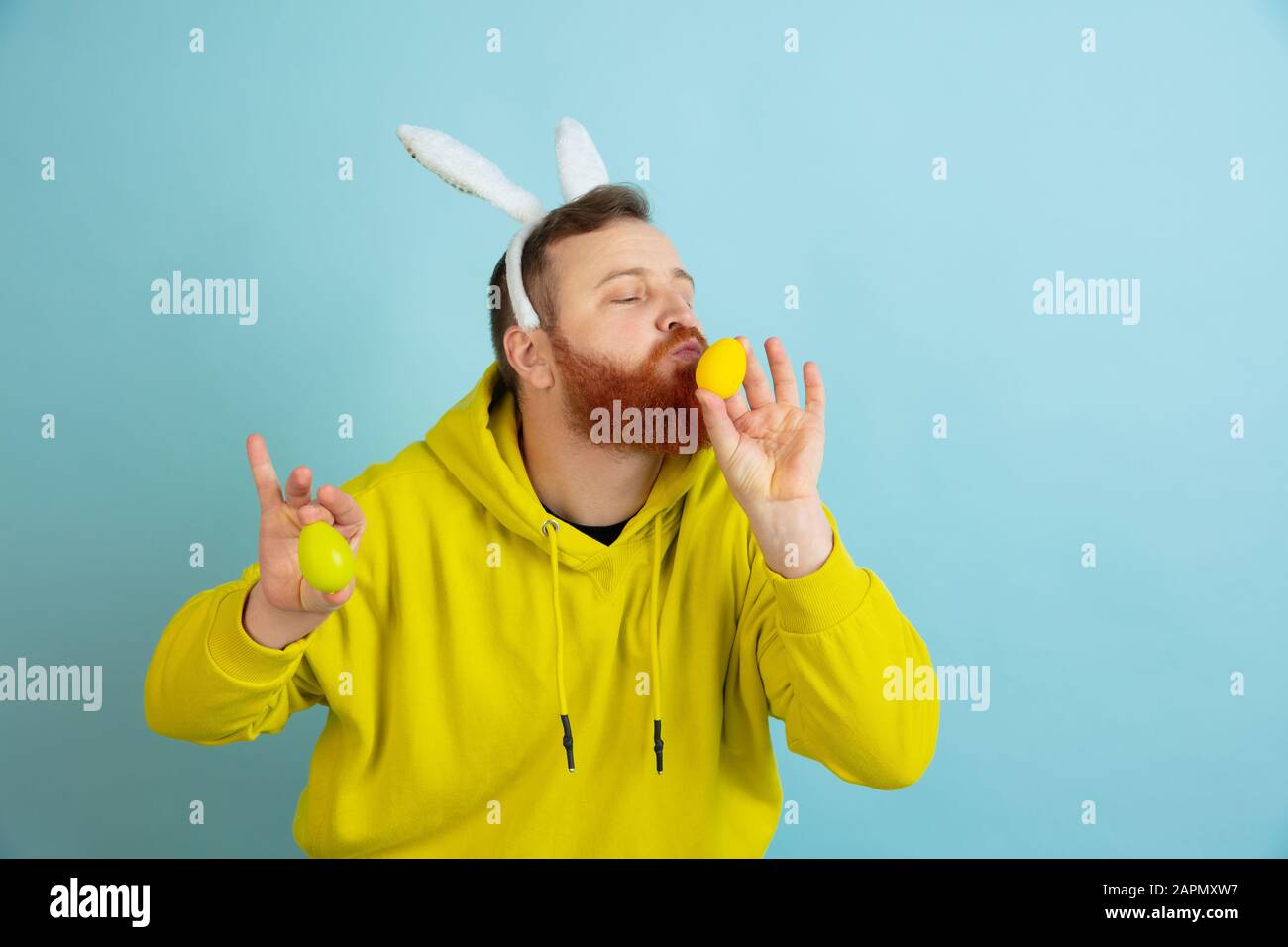 Chasse aux œufs à venir. Homme caucasien comme lapin de Pâques avec des vêtements décontractés lumineux sur fond bleu studio. Joyeuses salutations de pâques. Concept d'émotions humaines, d'expression faciale, de vacances. Copyspace. Banque D'Images