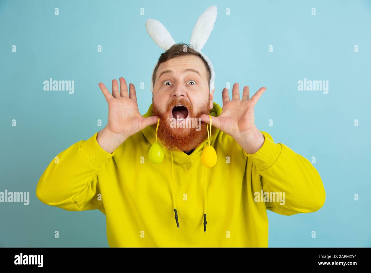 Chasse aux œufs à venir. Homme caucasien comme lapin de Pâques avec des vêtements décontractés lumineux sur fond bleu studio. Joyeuses salutations de pâques. Concept d'émotions humaines, d'expression faciale, de vacances. Copyspace. Banque D'Images