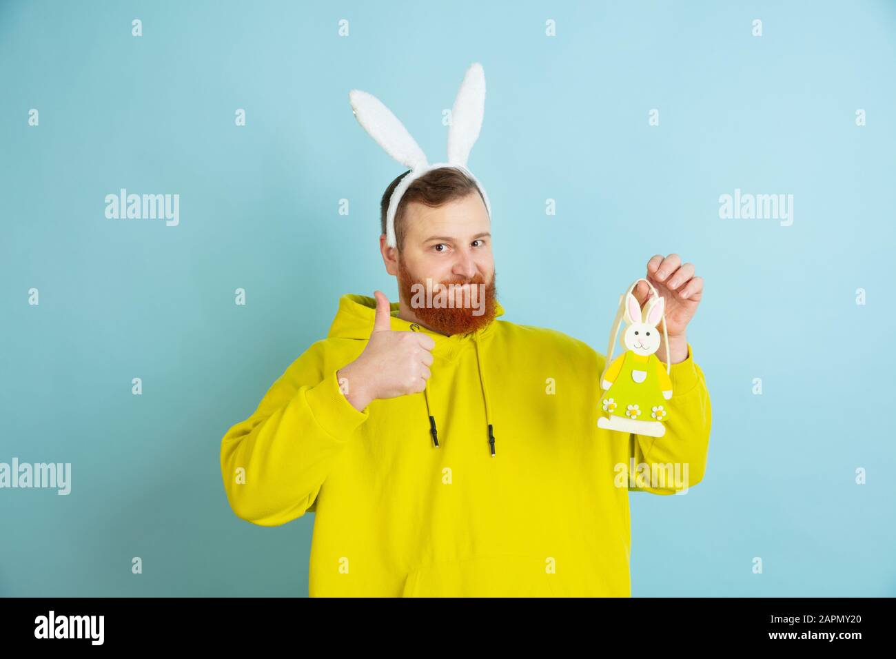 Pointant sur la décoration. Homme caucasien comme lapin de Pâques avec des vêtements décontractés lumineux sur fond bleu studio. Joyeuses salutations de pâques. Concept d'émotions humaines, d'expression faciale, de vacances. Copyspace. Banque D'Images