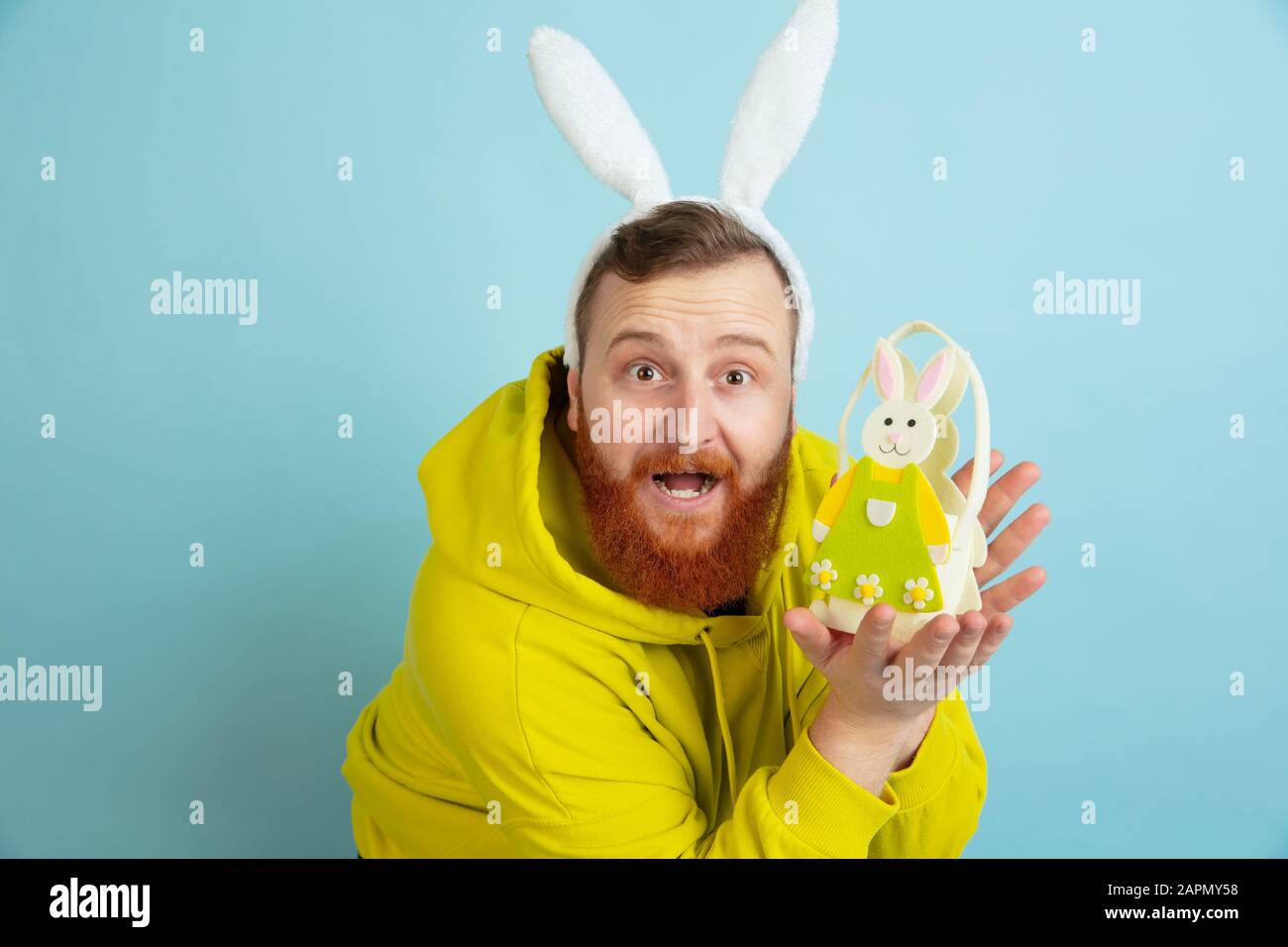 Décoration traditionnelle. Homme caucasien comme lapin de Pâques avec des vêtements décontractés lumineux sur fond bleu studio. Joyeuses salutations de pâques. Concept d'émotions humaines, d'expression faciale, de vacances. Copyspace. Banque D'Images