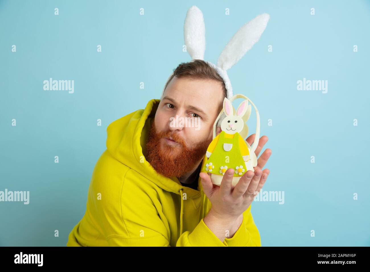 Décoration traditionnelle. Homme caucasien comme lapin de Pâques avec des vêtements décontractés lumineux sur fond bleu studio. Joyeuses salutations de pâques. Concept d'émotions humaines, d'expression faciale, de vacances. Copyspace. Banque D'Images