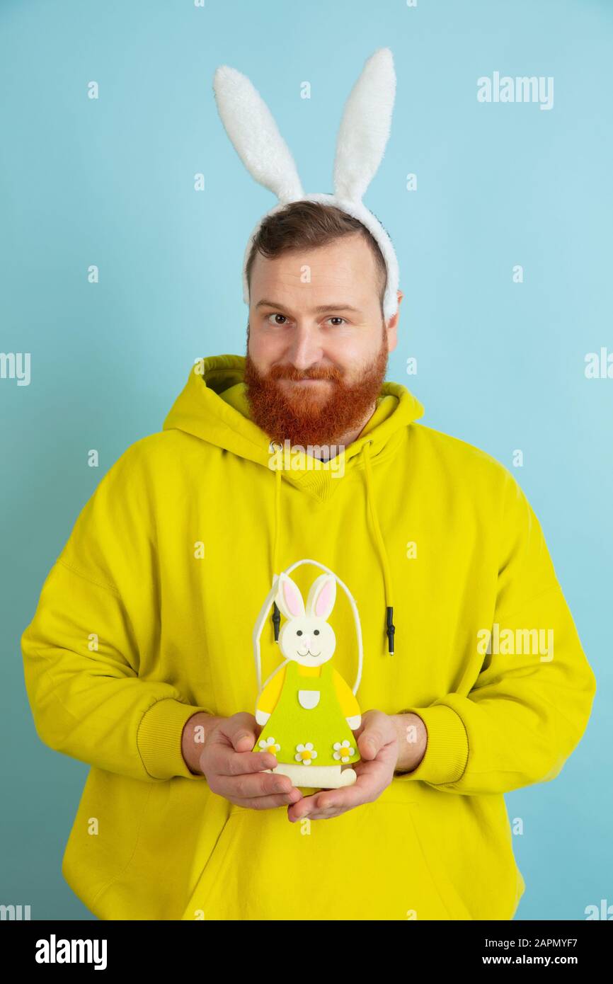 Décoration traditionnelle. Homme caucasien comme lapin de Pâques avec des vêtements décontractés lumineux sur fond bleu studio. Joyeuses salutations de pâques. Concept d'émotions humaines, d'expression faciale, de vacances. Copyspace. Banque D'Images