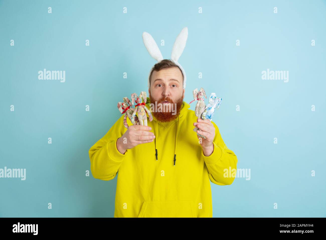 Décoration traditionnelle. Homme caucasien comme lapin de Pâques avec des vêtements décontractés lumineux sur fond bleu studio. Joyeuses salutations de pâques. Concept d'émotions humaines, d'expression faciale, de vacances. Copyspace. Banque D'Images