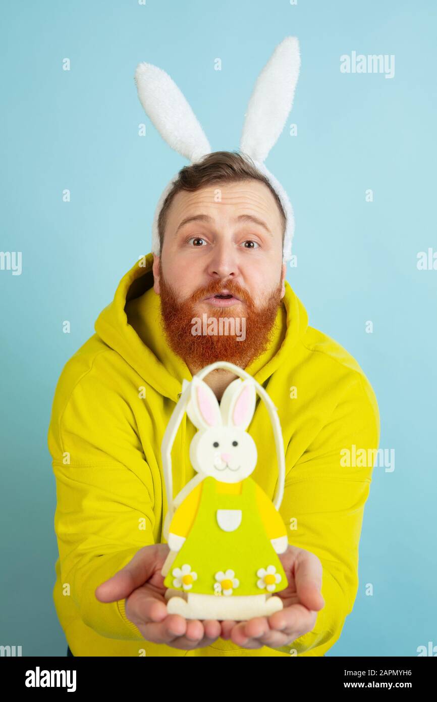 Décoration traditionnelle. Homme caucasien comme lapin de Pâques avec des vêtements décontractés lumineux sur fond bleu studio. Joyeuses salutations de pâques. Concept d'émotions humaines, d'expression faciale, de vacances. Copyspace. Banque D'Images