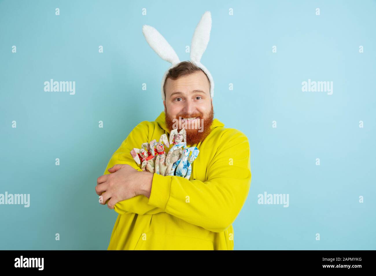 Décoration traditionnelle. Homme caucasien comme lapin de Pâques avec des vêtements décontractés lumineux sur fond bleu studio. Joyeuses salutations de pâques. Concept d'émotions humaines, d'expression faciale, de vacances. Copyspace. Banque D'Images