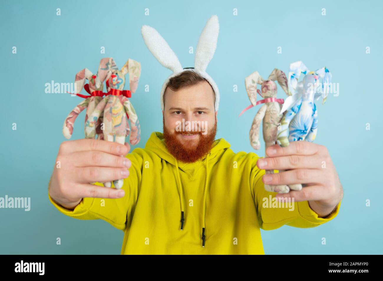 Décoration traditionnelle. Homme caucasien comme lapin de Pâques avec des vêtements décontractés lumineux sur fond bleu studio. Joyeuses salutations de pâques. Concept d'émotions humaines, d'expression faciale, de vacances. Copyspace. Banque D'Images