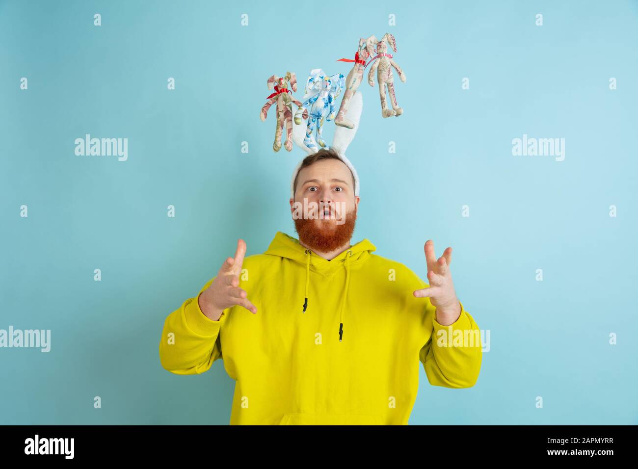 Décoration traditionnelle. Homme caucasien comme lapin de Pâques avec des vêtements décontractés lumineux sur fond bleu studio. Joyeuses salutations de pâques. Concept d'émotions humaines, d'expression faciale, de vacances. Copyspace. Banque D'Images