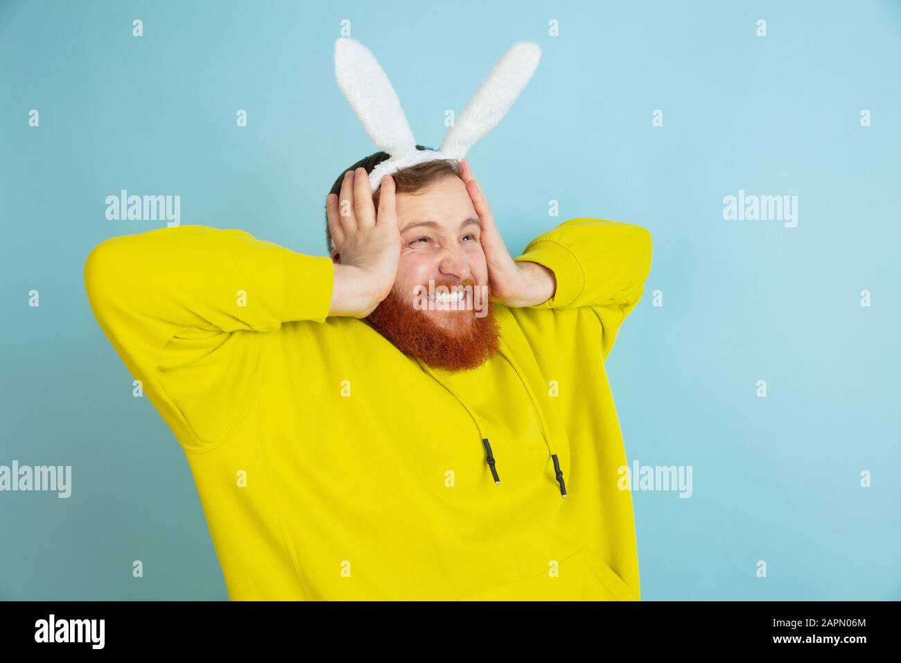 Choqué, étonné. Homme caucasien comme lapin de Pâques avec des vêtements décontractés lumineux sur fond bleu studio. Joyeuses salutations de pâques. Concept d'émotions humaines, d'expression faciale, de vacances. Copyspace. Banque D'Images