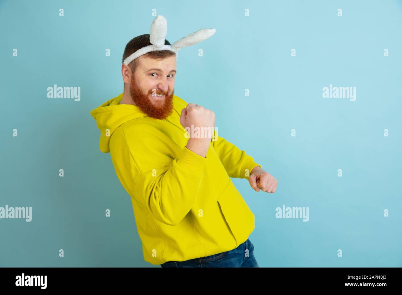 Célèbre comme gagnant. Homme caucasien comme lapin de Pâques avec des vêtements décontractés lumineux sur fond bleu studio. Joyeuses salutations de pâques. Concept d'émotions humaines, d'expression faciale, de vacances. Copyspace. Banque D'Images