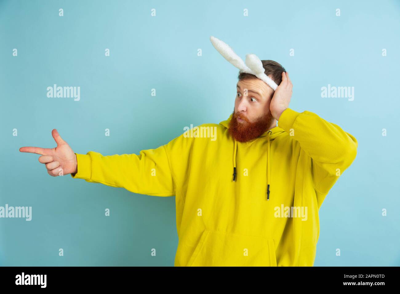 Orienté vers le côté. Homme caucasien comme lapin de Pâques avec des vêtements décontractés lumineux sur fond bleu studio. Joyeuses salutations de pâques. Concept d'émotions humaines, d'expression faciale, de vacances. Copyspace. Banque D'Images
