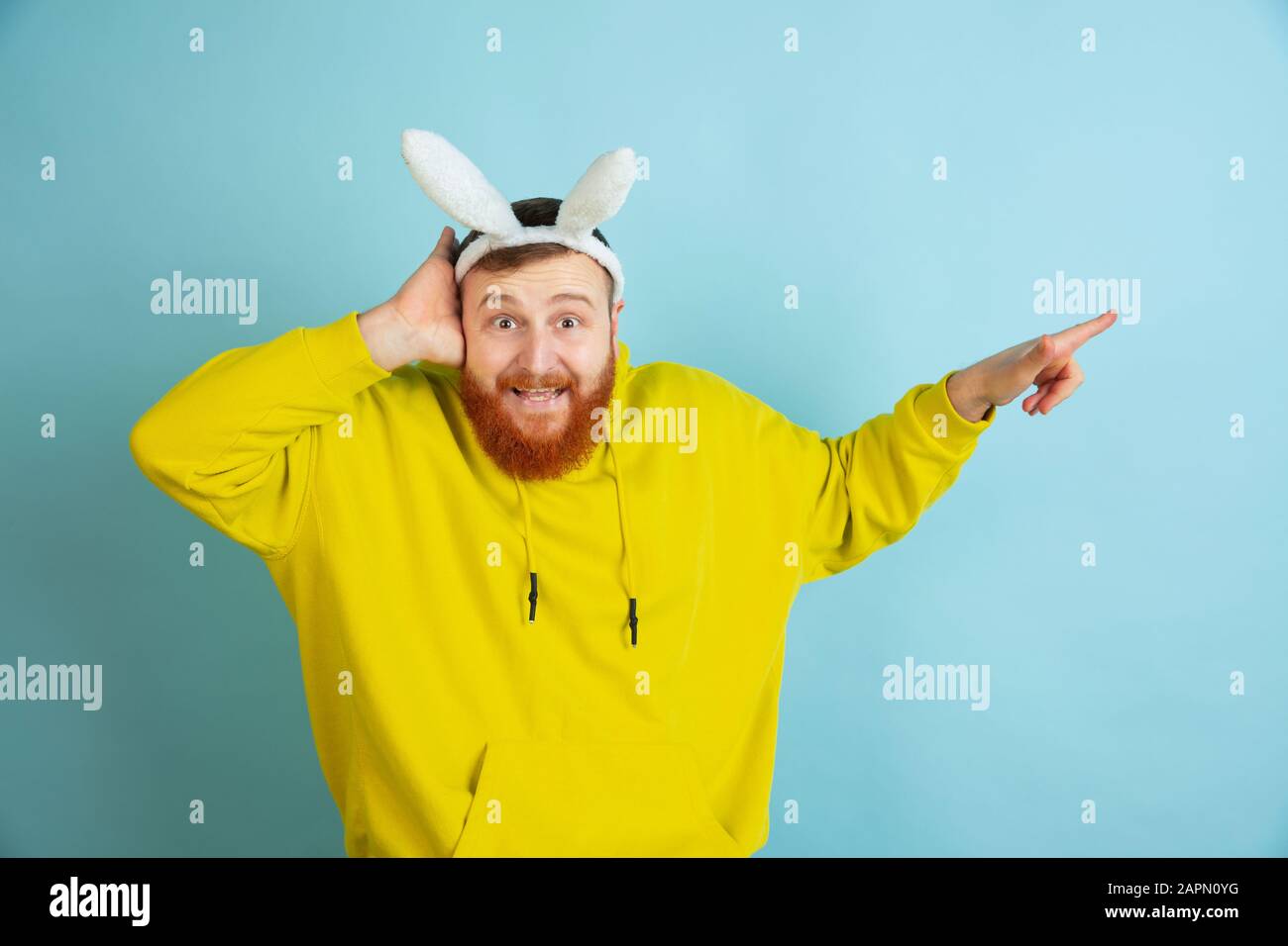Orienté vers le côté. Homme caucasien comme lapin de Pâques avec des vêtements décontractés lumineux sur fond bleu studio. Joyeuses salutations de pâques. Concept d'émotions humaines, d'expression faciale, de vacances. Copyspace. Banque D'Images