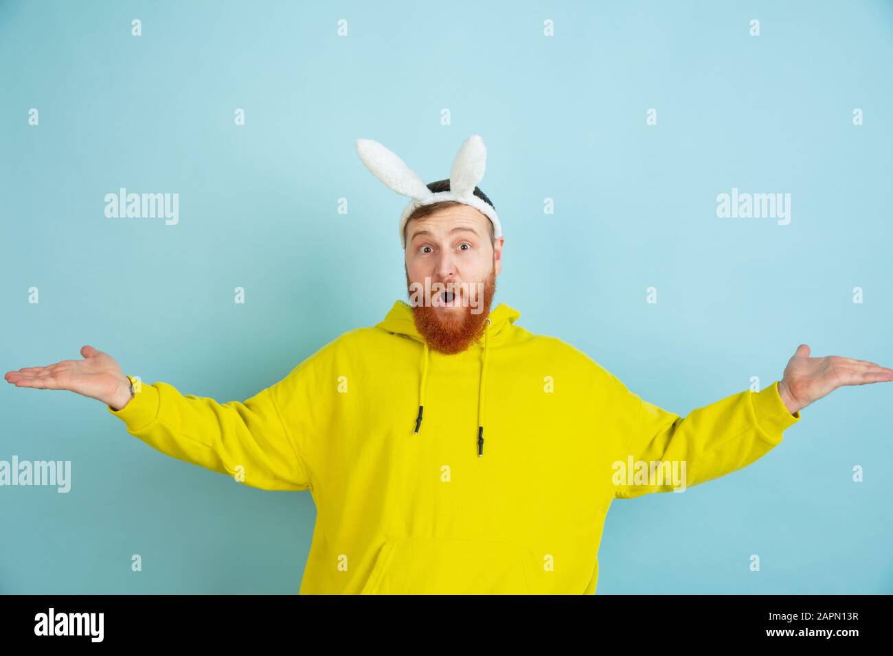 Invitation, accueil. Homme caucasien comme lapin de Pâques avec des vêtements décontractés lumineux sur fond bleu studio. Joyeuses salutations de pâques. Concept d'émotions humaines, d'expression faciale, de vacances. Copyspace. Banque D'Images