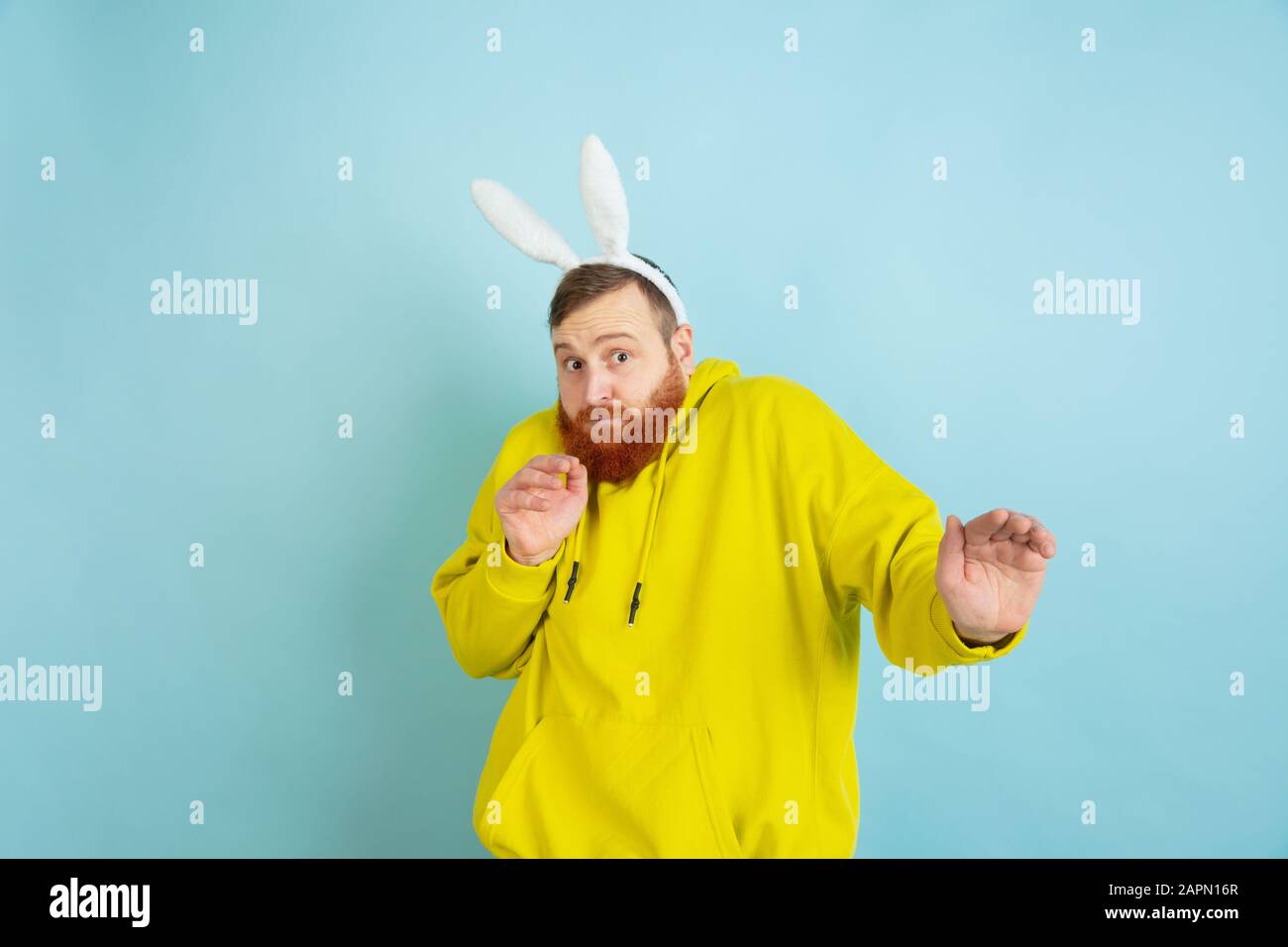 Peur, rejet. Homme caucasien comme lapin de Pâques avec des vêtements décontractés lumineux sur fond bleu studio. Joyeuses salutations de pâques. Concept d'émotions humaines, d'expression faciale, de vacances. Copyspace. Banque D'Images