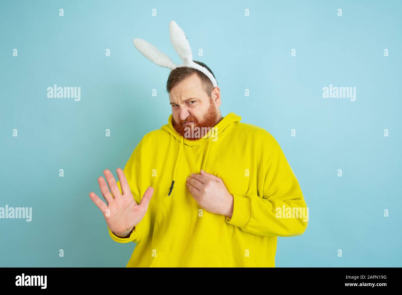 Peur, rejet. Homme caucasien comme lapin de Pâques avec des vêtements décontractés lumineux sur fond bleu studio. Joyeuses salutations de pâques. Concept d'émotions humaines, d'expression faciale, de vacances. Copyspace. Banque D'Images