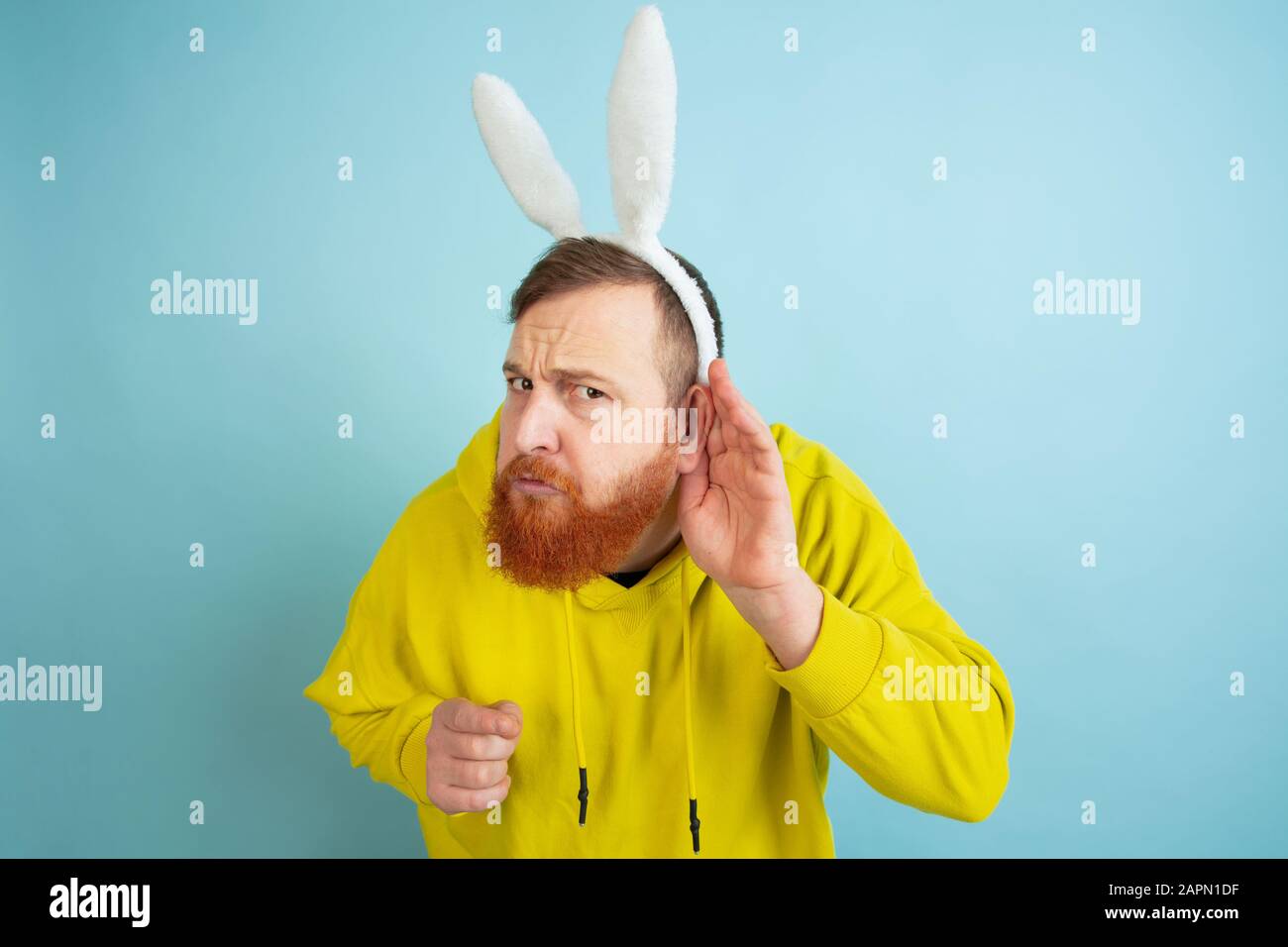 Ecouter le secret. Homme caucasien comme lapin de Pâques avec des vêtements décontractés lumineux sur fond bleu studio. Joyeuses salutations de pâques. Concept d'émotions humaines, d'expression faciale, de vacances. Copyspace. Banque D'Images