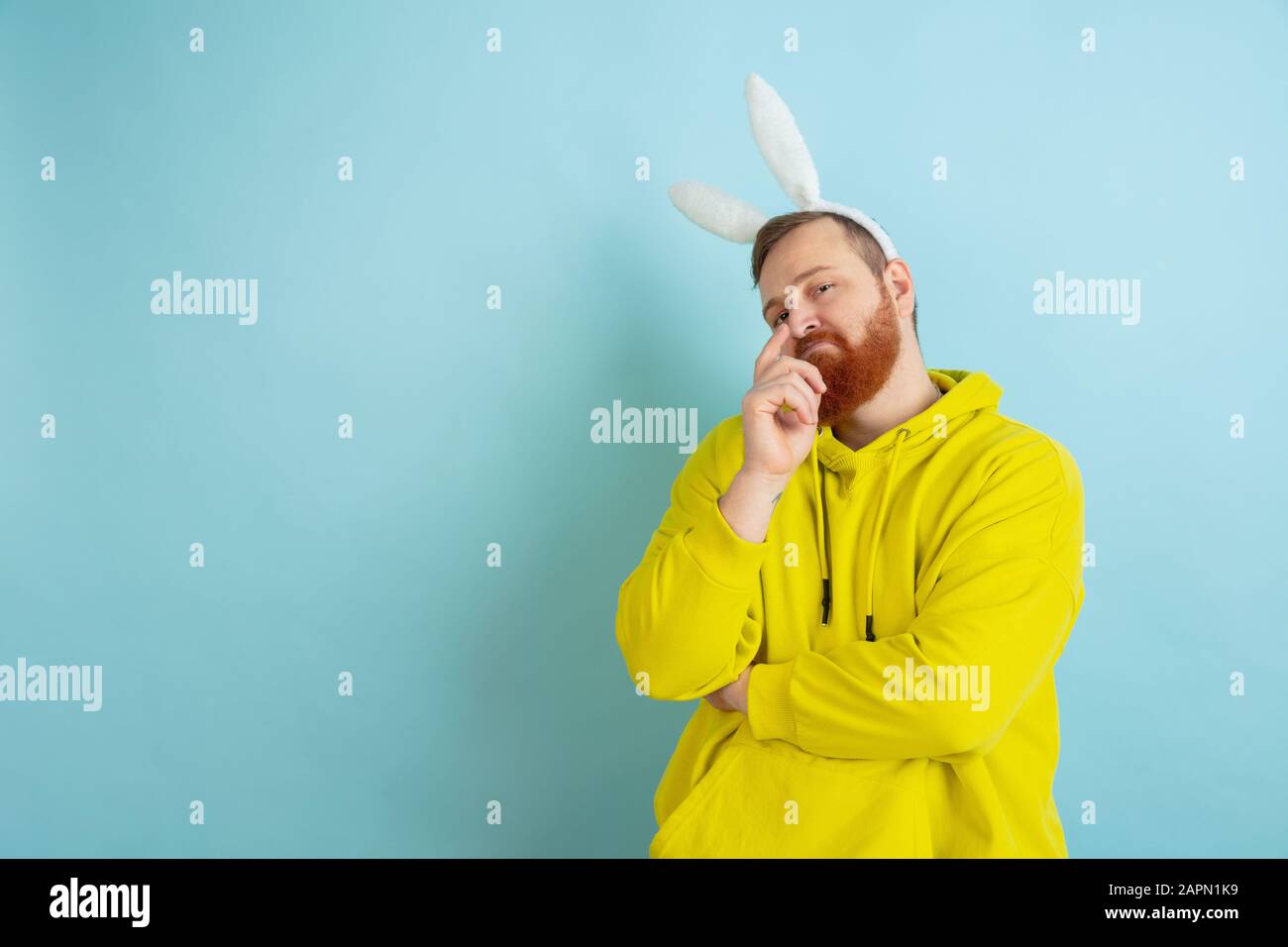 Confiant, pensant. Homme caucasien comme lapin de Pâques avec des vêtements décontractés lumineux sur fond bleu studio. Joyeuses salutations de pâques. Concept d'émotions humaines, d'expression faciale, de vacances. Copyspace. Banque D'Images