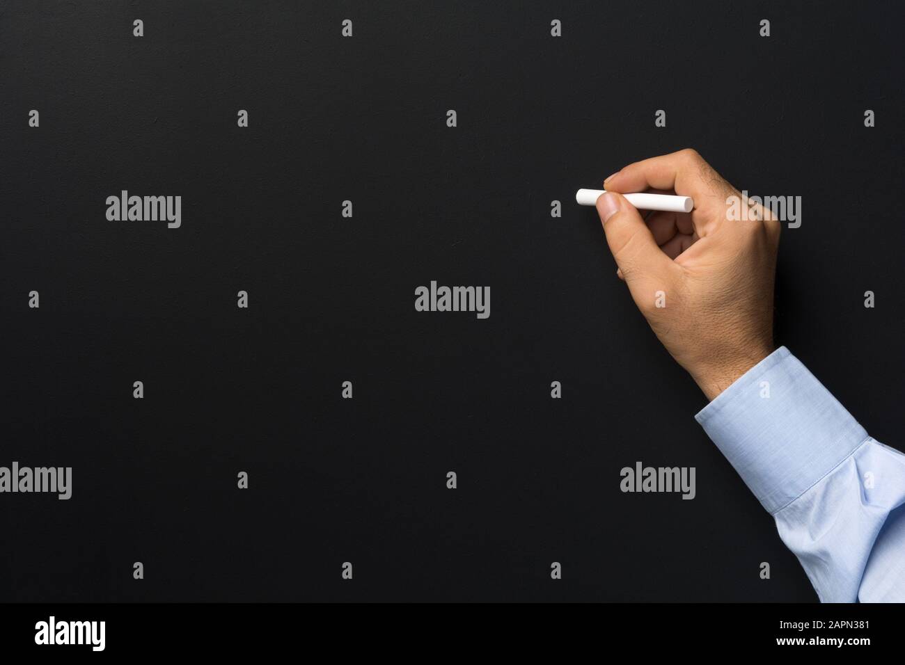 Gros plan sur la craie de la main de l'homme contre le tableau noir blanc Banque D'Images