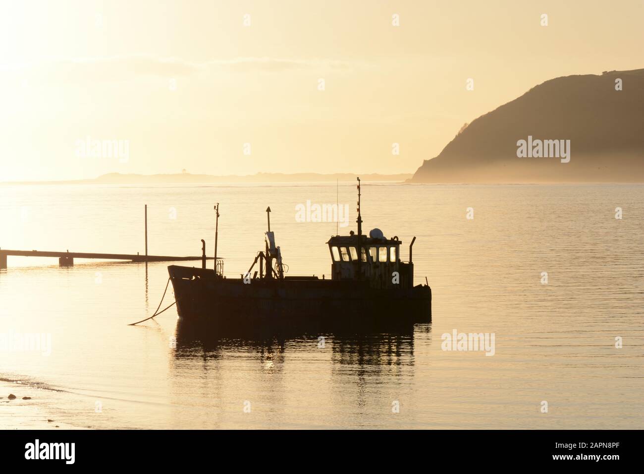 Vieux bateau de pêche silhouetted dans misty début de soirée coucher de soleil coucher de soleil Tywi Estuaire Ferryside Carmarthenshire Pays de Galles Cymru Royaume-Uni Banque D'Images