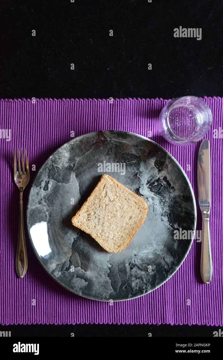 Repas réduit en Carême avec une tranche de pain sur une plaque et un verre d'eau Banque D'Images