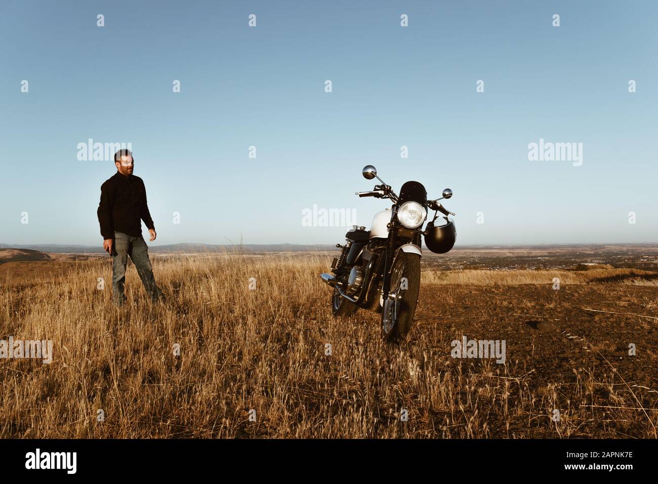 Homme et moto vintage dans le pays au coucher du soleil. Banque D'Images