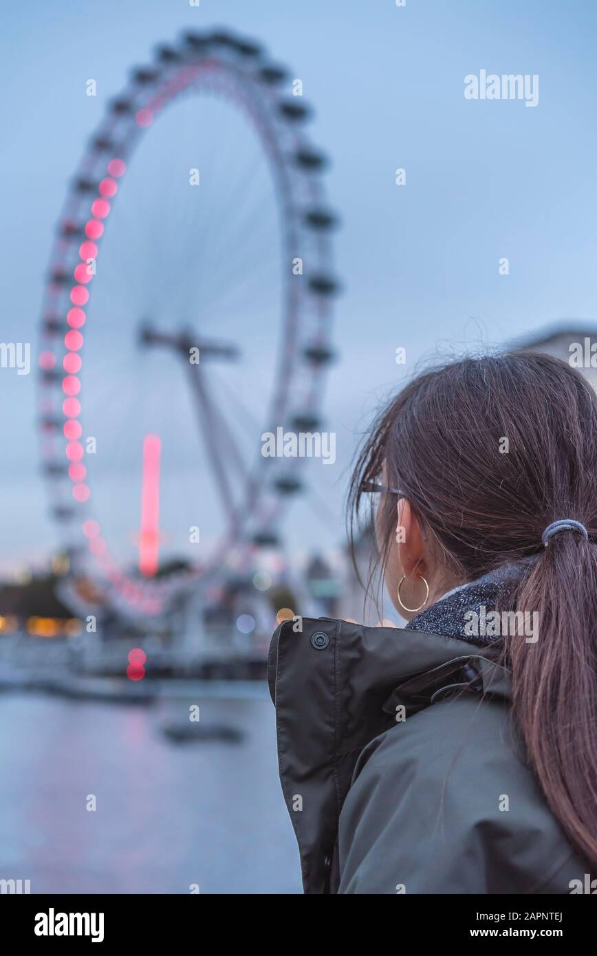 Vue arrière en soirée d'une femme isolée sur le pont de Westminster en regardant le célèbre monument du London Eye, Millennium Wheel, Londres, Royaume-Uni. Banque D'Images
