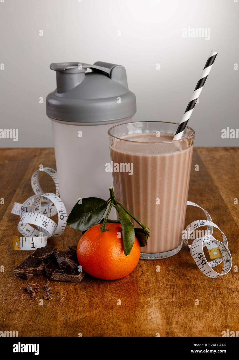 Milk-shake chocolat orange, ingrédients, mètre à ruban et agitateur avec paille de papier sur un plan de travail en bois Banque D'Images