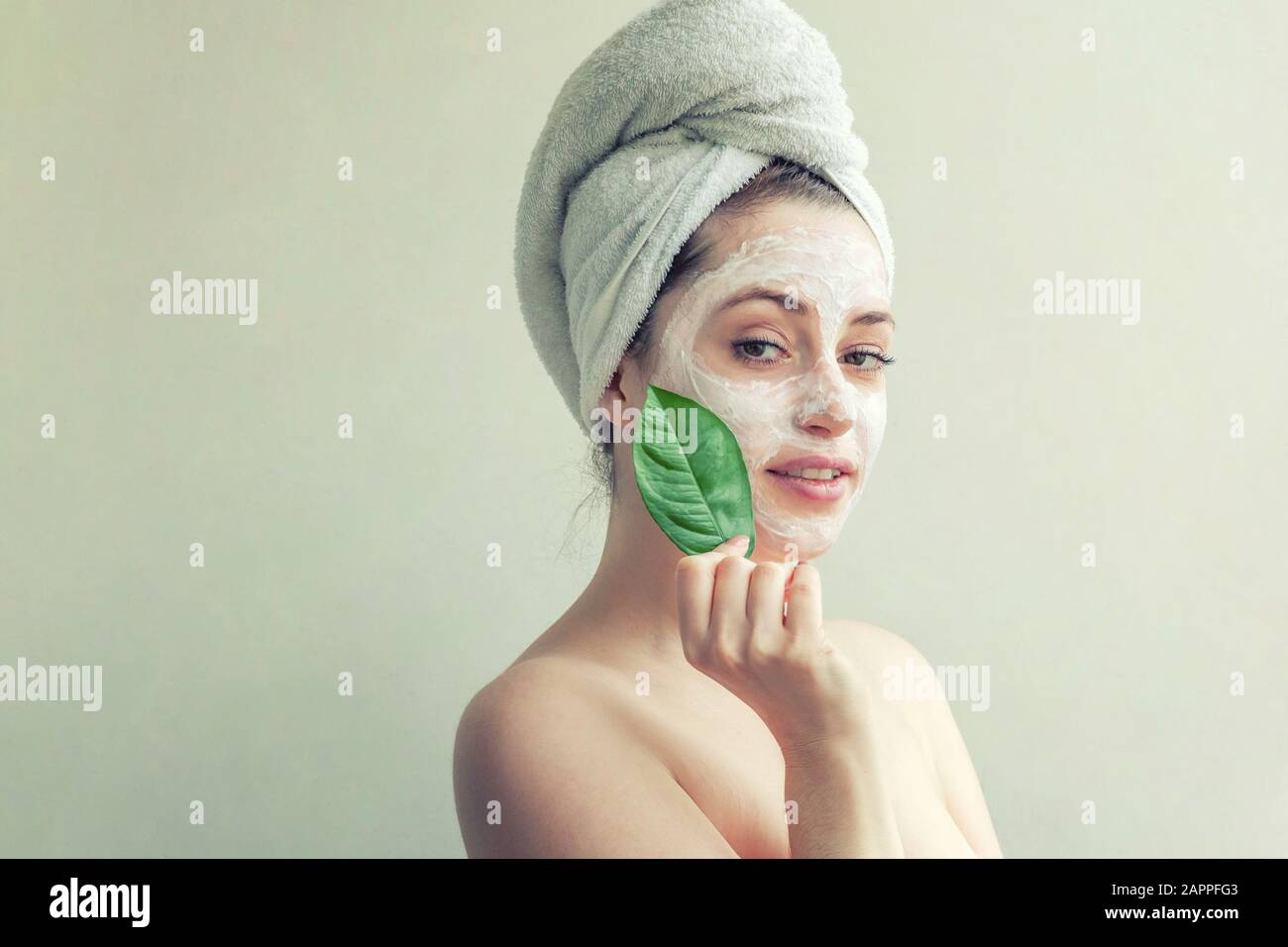 Portrait of woman in towel on head avec blanc masque nourrissant ou la crème sur le visage et le vert feuille dans la main, fond blanc isolé. Nettoyage de la peau cosmétiques bio eco spa concept Banque D'Images