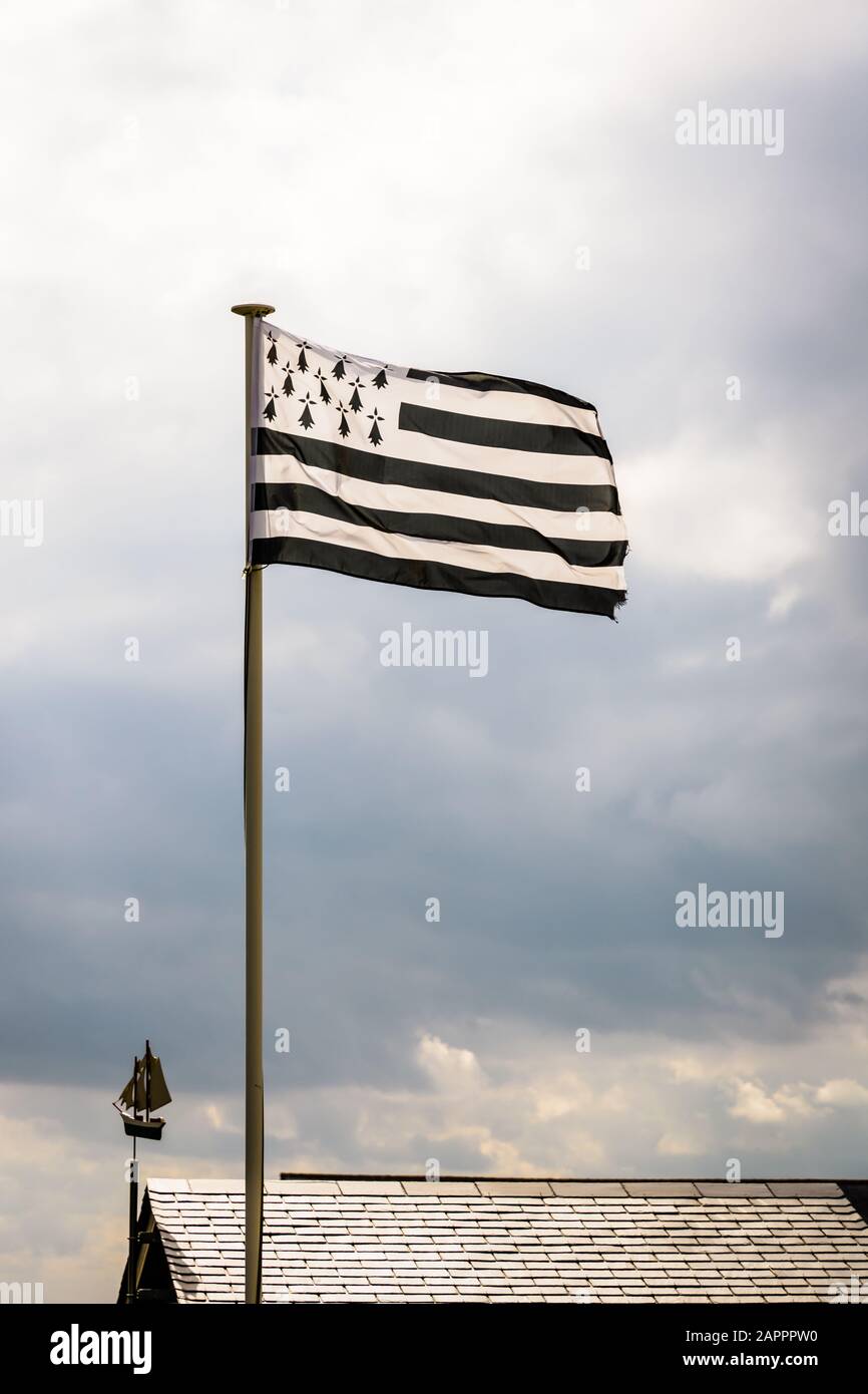 Drapeau de Bretagne, nommé Gwenn ha du en Breton, volant au-dessus d'un toit en ardoise avec une girouette sous forme de bateau à voile contre un ciel de tempête. Banque D'Images