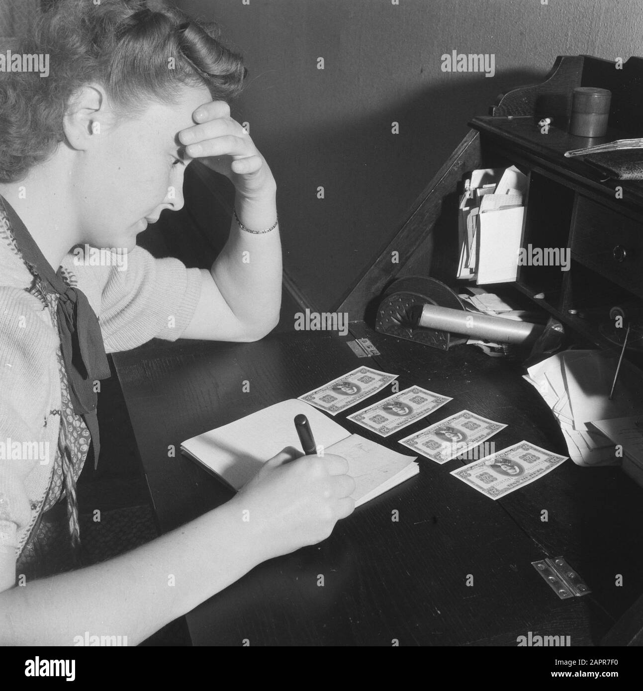 Finances : Purger L'Argent Purger L'Argent. Une femme écrit quelque chose dans un bloc-notes. Devant elle se trouvent quatre billets d'un Rijksdaalder (2 1/2 guilder) Date: 1945 mots clés: Financier, argent Banque D'Images