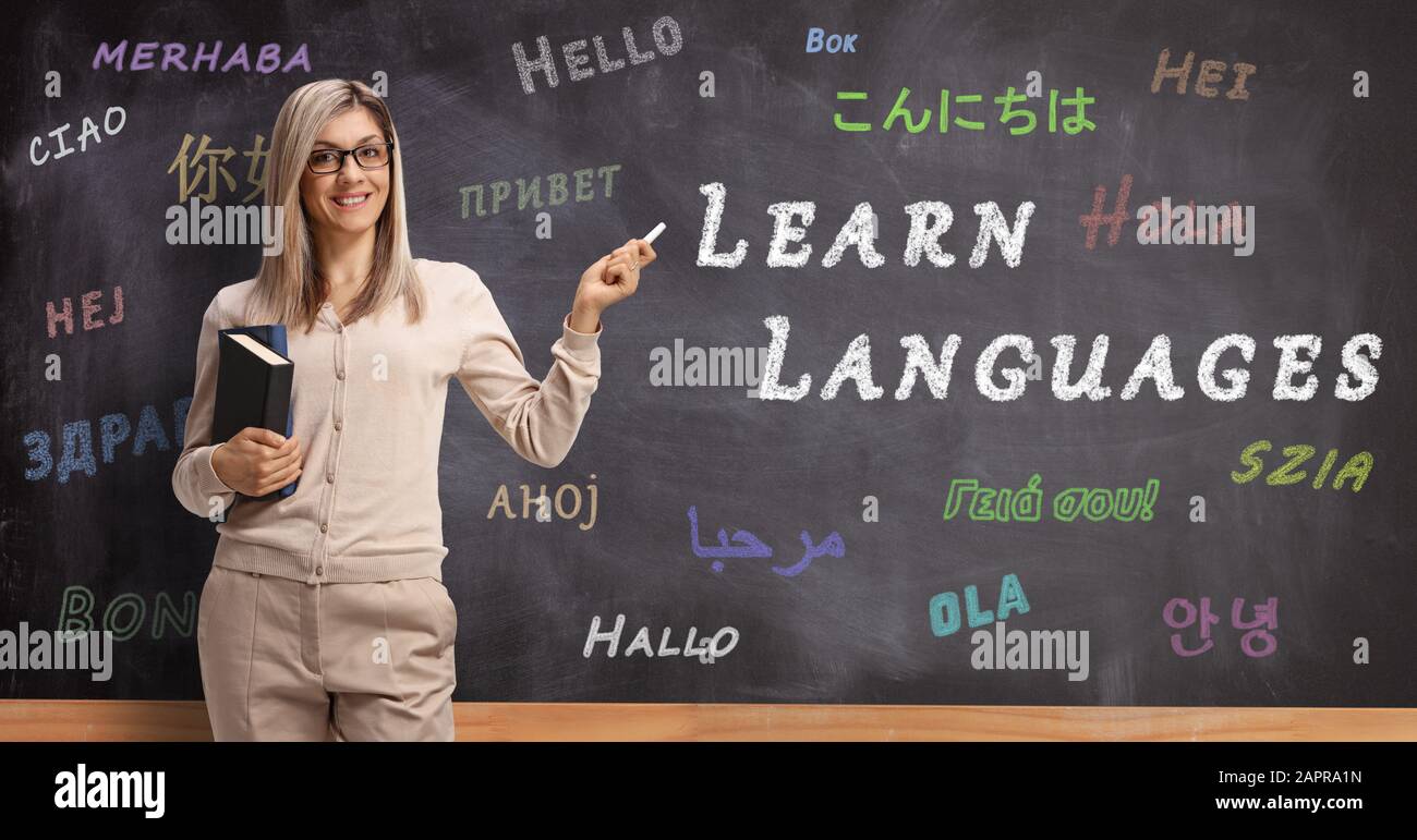 Professeur de langue anglaise debout devant un tableau noir avec bonjour écrit dans différentes langues et pointant avec craie à un texte d'apprentissage des langues Banque D'Images