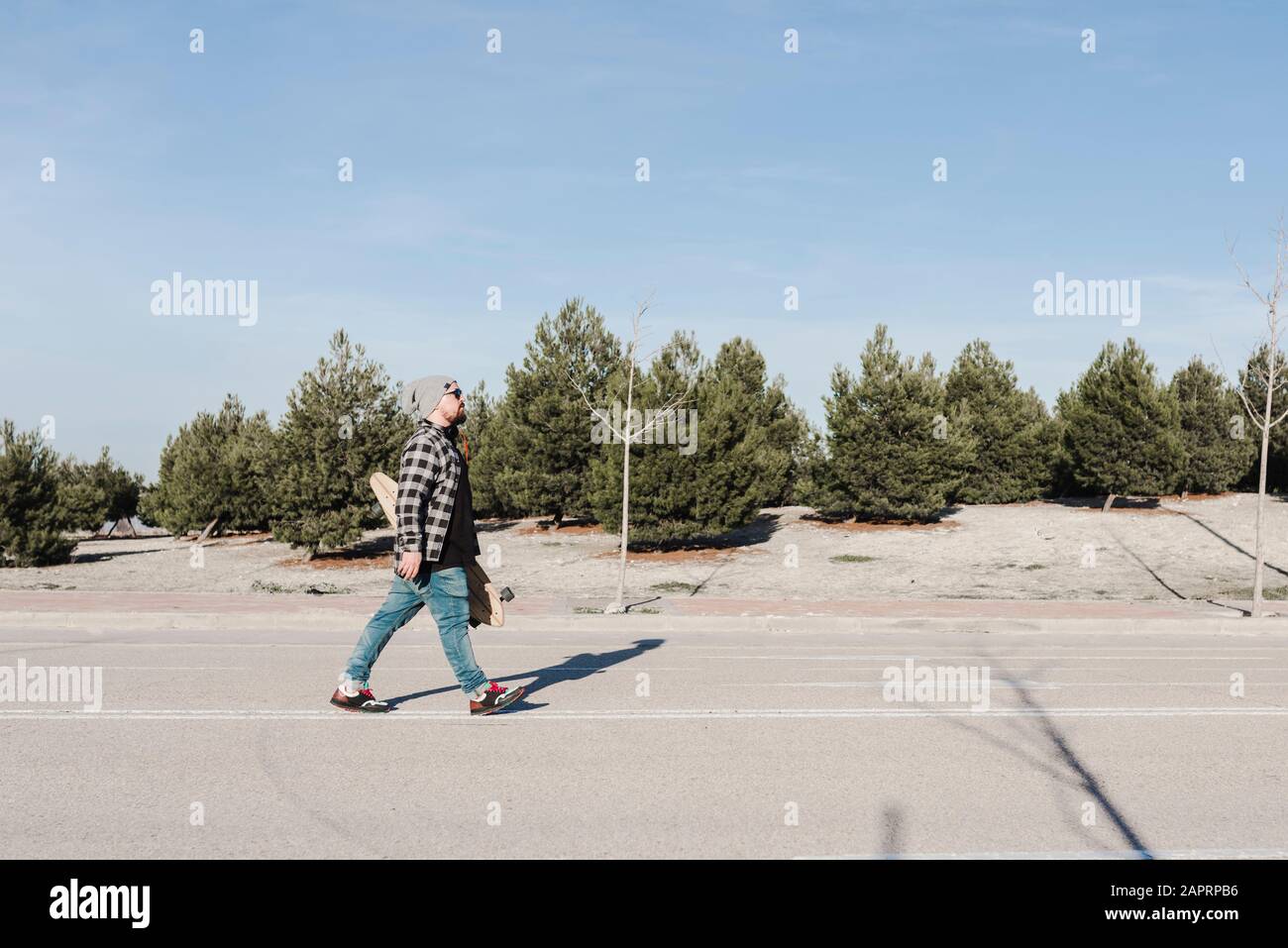 Jeune homme moderne marchant avec son longboard Banque D'Images