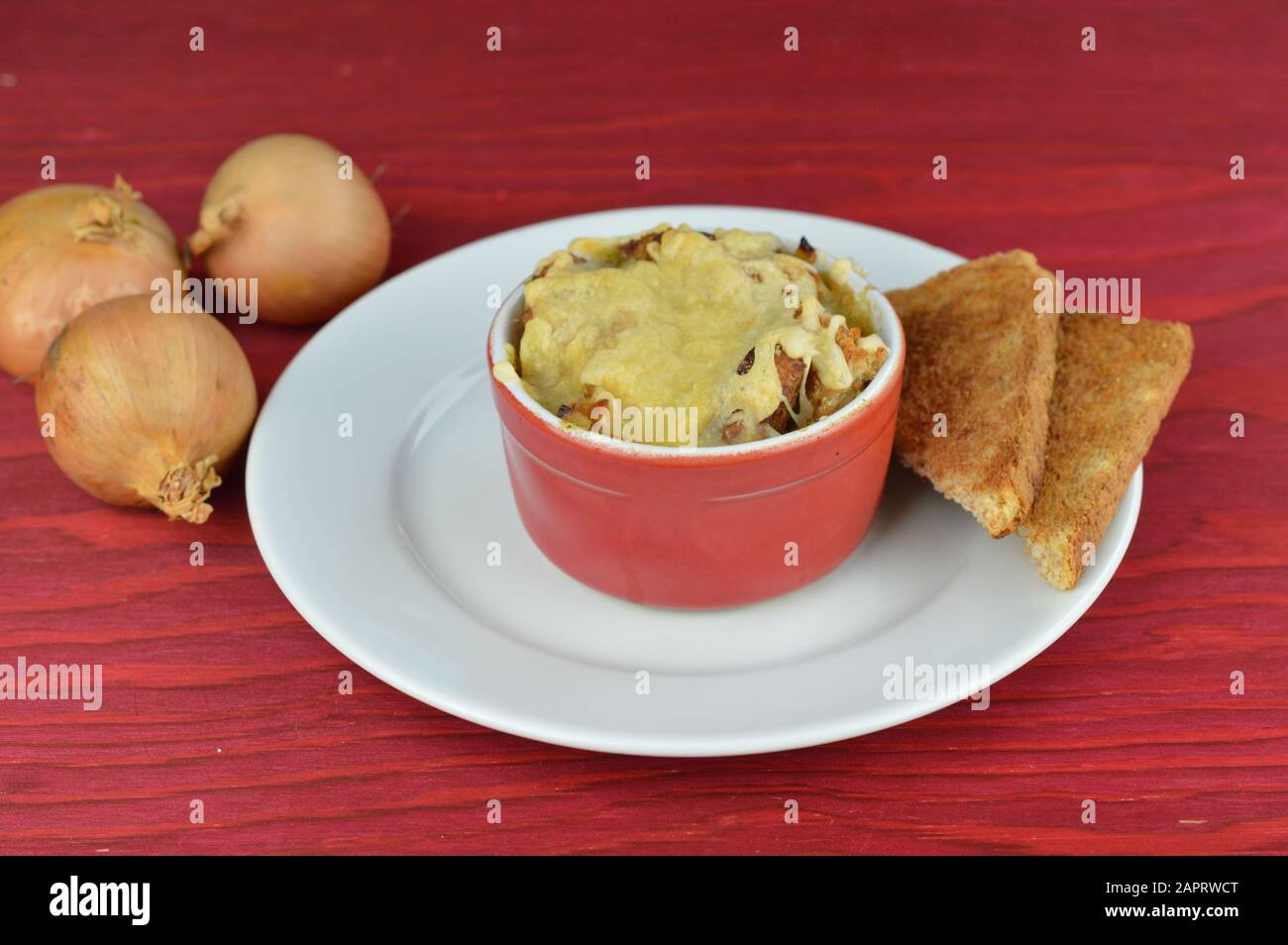 soupe à l'oignon au gratin avec pain et fromage sur table en bois rouge avec oignons à côté comme nourriture traditionnelle d'automne Banque D'Images