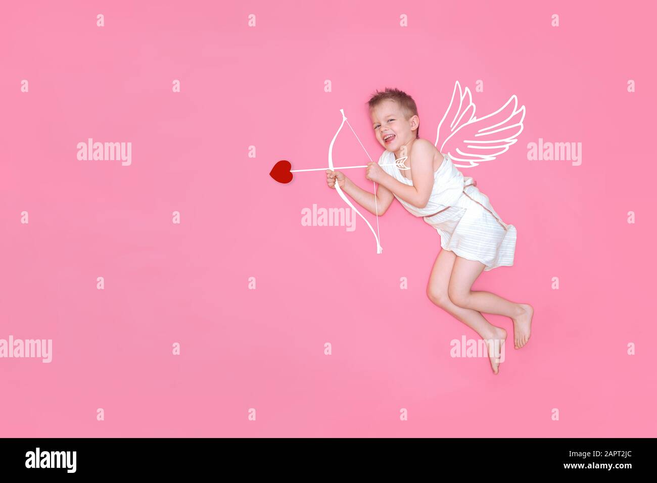 Heureux sourire bébé cupid dans les ailes d'ange de costume, arc et la flèche de coeur isolé sur fond de studio rose. CopySpace pour le texte. Concept de Saint Valentin Banque D'Images