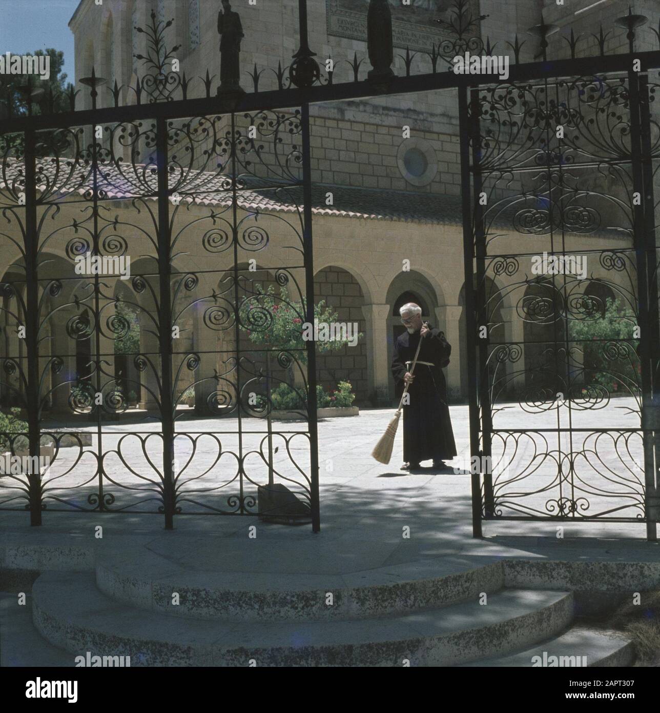 Ein Kerem. Église de la Visitation : un prêtre franciscain balaie la place près de l'église. Au premier plan une clôture en fer forgé Date : 1 janvier 1964 lieu : Ein Karem, Israël mots clés : Franciscains, clergymen, clôtures, édifices religieux, monastère, places Banque D'Images