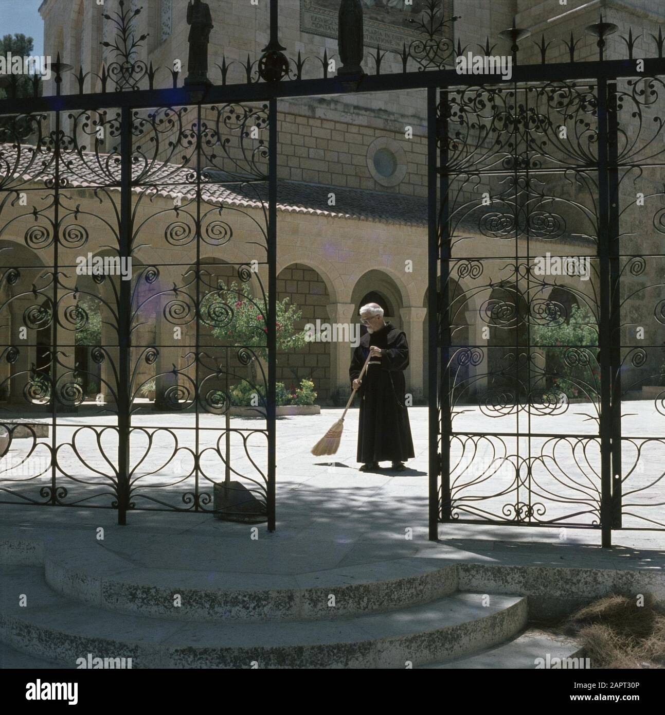 Ein Kerem. Église de la Visitation : un prêtre franciscain balaie la place près de l'église. Au premier plan une clôture en fer forgé Date : 1 janvier 1964 lieu : Ein Karem, Israël mots clés : Franciscains, clergymen, clôtures, édifices religieux, monastère, places Banque D'Images
