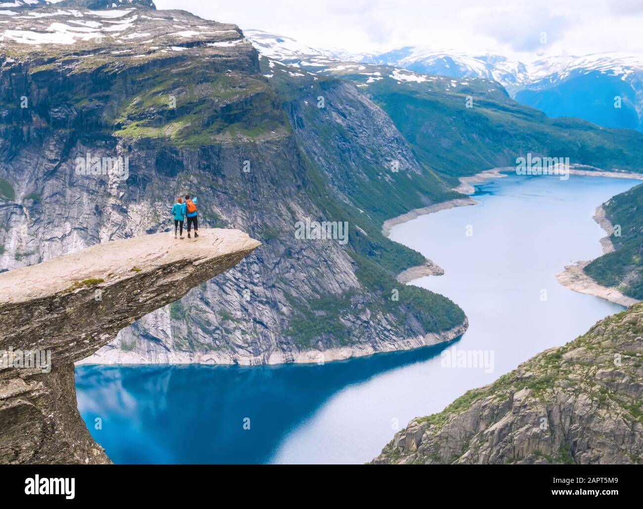 Couple posing sur Trolltunga. La femme et l'homme heureux profiter du magnifique lac et de beau temps en Norvège. Banque D'Images