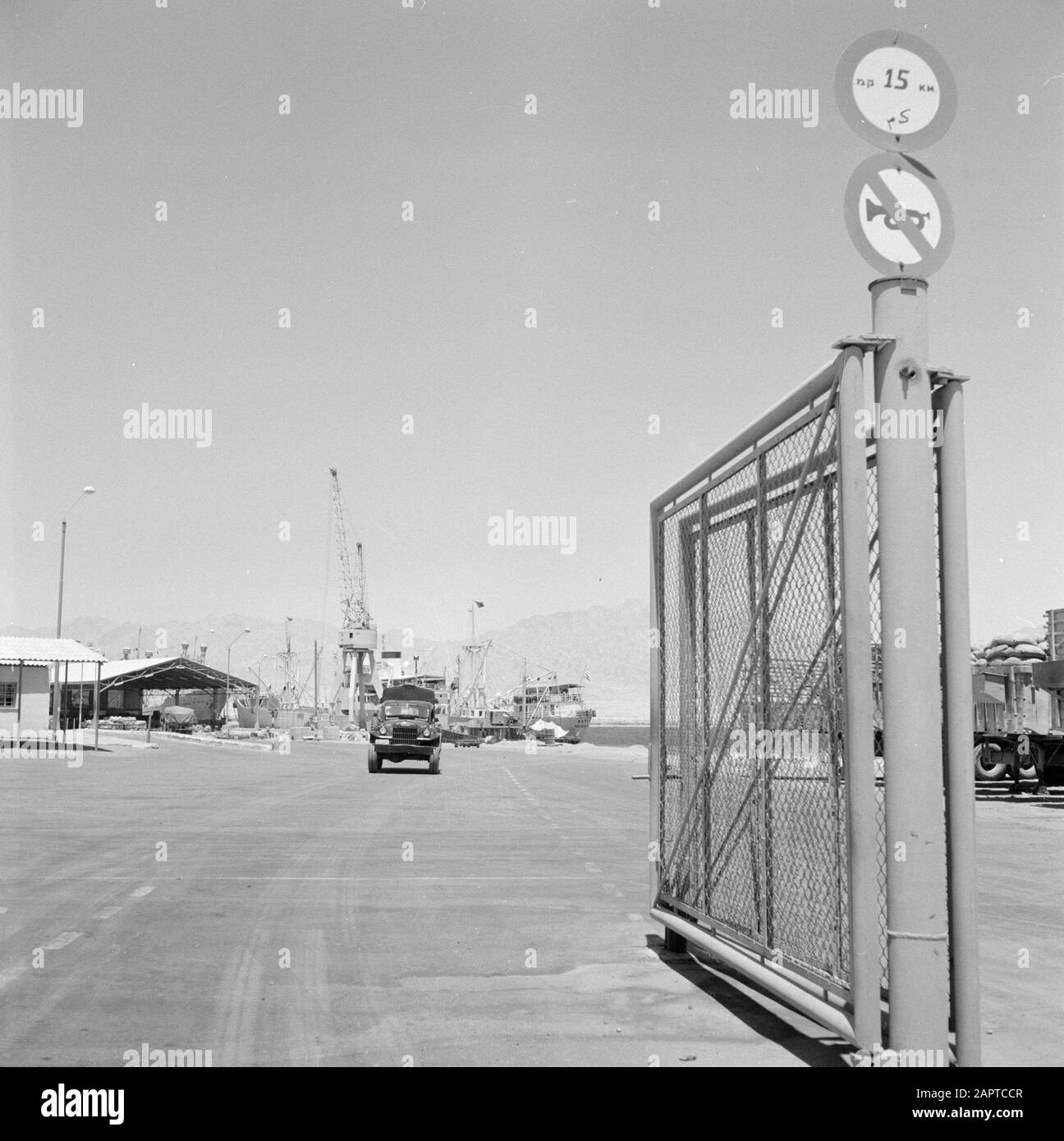 Vue sur la zone portuaire d'Eilat avec des navires amarrés et les installations portuaires qui y sont présentes. Au premier plan une clôture avec des panneaux pour le trafic automobile Date: 1 janvier 1963 lieu: Eilat, Golfe d'Aqaba, Israël mots clés: Ports, clôtures, grues, navires, panneaux routiers Banque D'Images