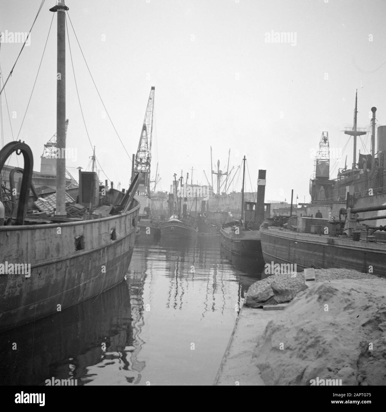 Port avec barges, remorqueurs, grues et un cargo en arrière-plan Date: Non daté mots clés: Barges, ports, navires de fret Banque D'Images