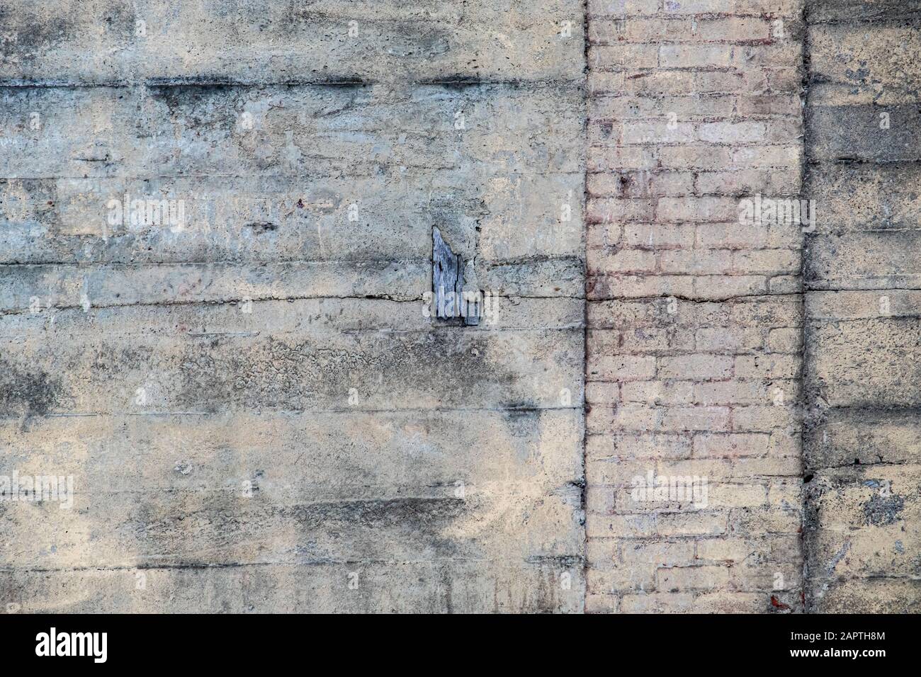 Une section d'un vieux mur de béton avec une colonne verticale de briques montre une variété de textures et de lignes où il a été patché et réparé. Banque D'Images