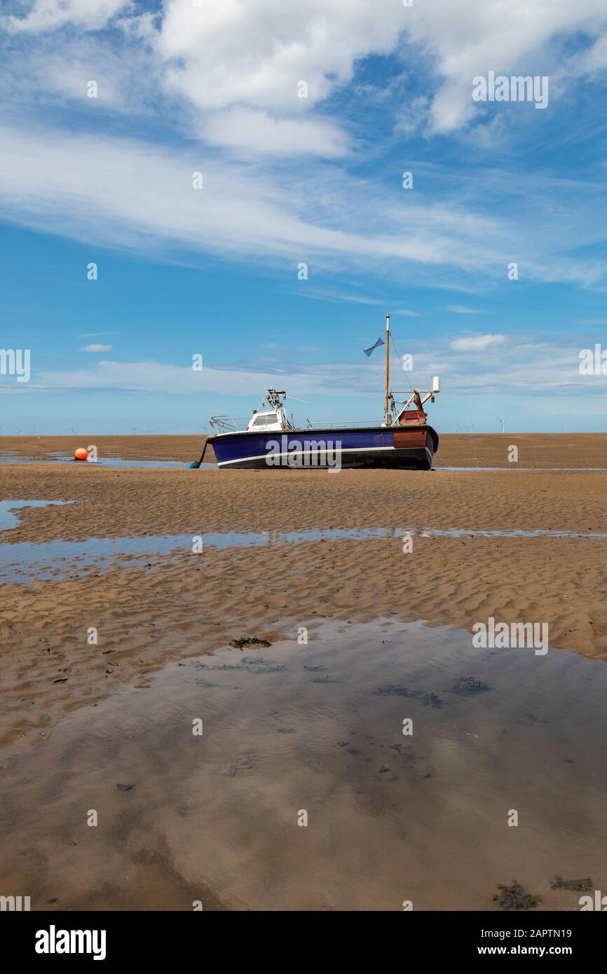 Petit bateau bleu et blanc amarré sur la plage à marée basse à Meols juin 2019 Banque D'Images