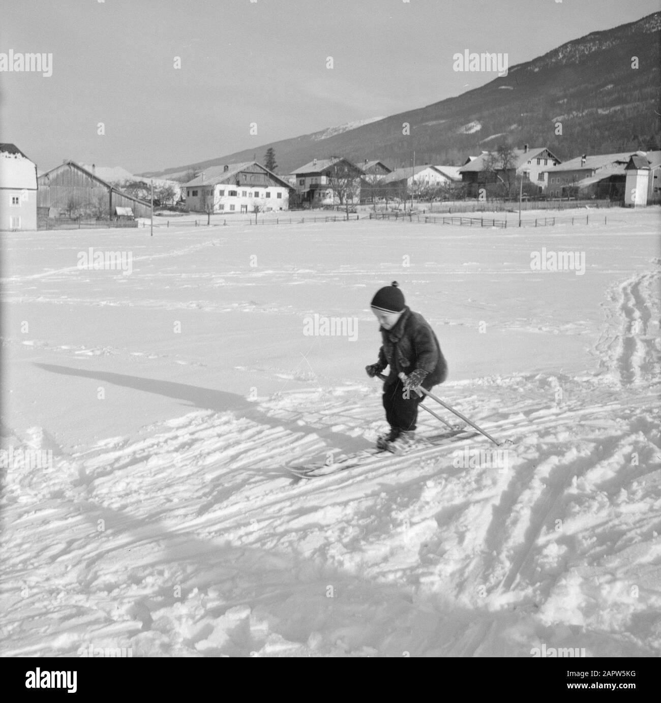 Hiver au Tyrol enfant avec skis dans la neige avec en arrière-plan Sistrans et les montagnes Karwendel Date: Janvier 1960 lieu: Autriche, Sistrans, Tyrol mots clés: Montagnes, villages, paysages, ski de fond, ski, neige, hiver, sports d'hiver Banque D'Images