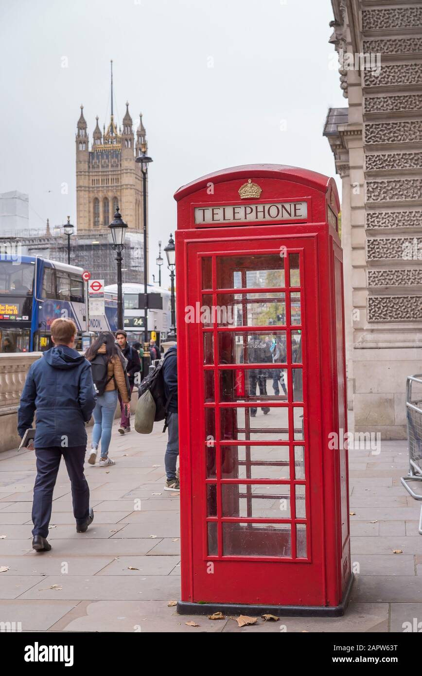 Boîte d'appel téléphonique rouge sur London Whitehall Street, Westminster (Royaume-Uni) ; Chambres du Parlement en arrière-plan et piétons occupés passant par le pavé. Banque D'Images