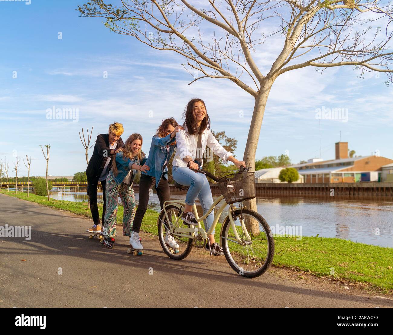 Quatre adolescents qui s'amusent à l'extérieur, à côté d'une rivière, avec patins à roulettes et vélo Banque D'Images