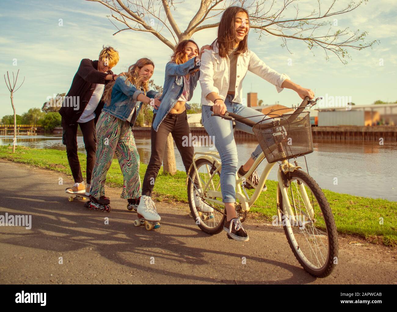 Quatre adolescents qui s'amusent à l'extérieur, à côté d'une rivière, avec patins à roulettes et vélo Banque D'Images